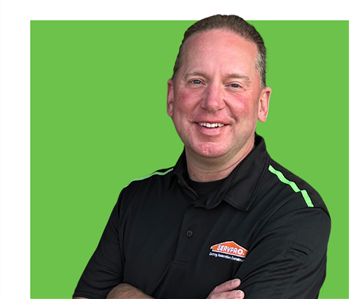 Hand with arms crossed over a black SERVPRO polo shirt